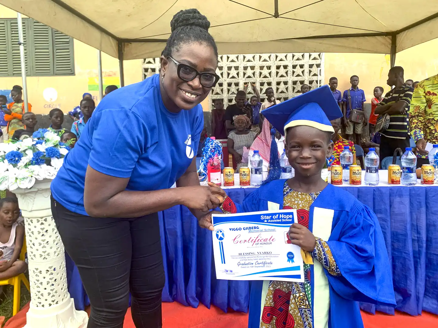 Kvinna delar ut diplom vid skolavslutning i Ghana