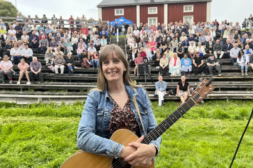 kvinna med gitarr framför publik.