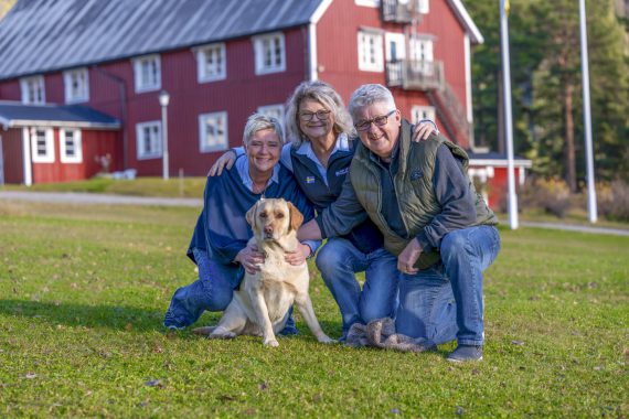 två kvinnor, en man, en hund på gräsmatta i sverige