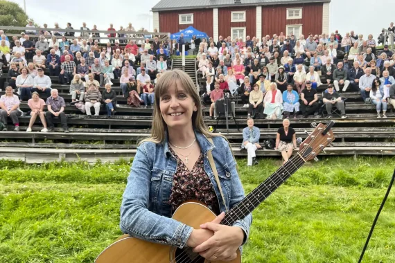 kvinna med gitarr framför publik.